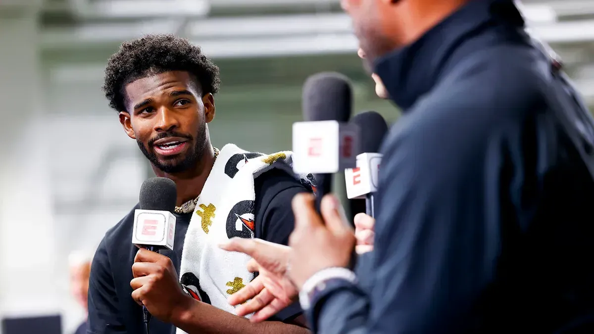 A man is talking into a microphone while another man looks on.