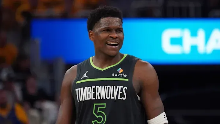 A basketball player wearing a timberwolves jersey is smiling during a game.