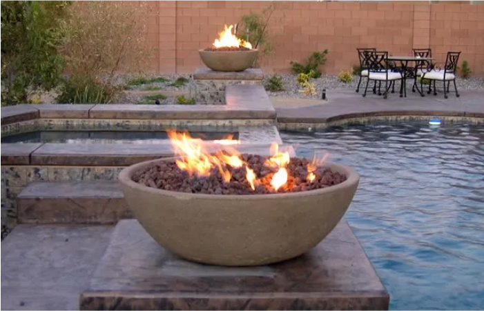 A fire pit in front of a pool with a table and chairs in the background