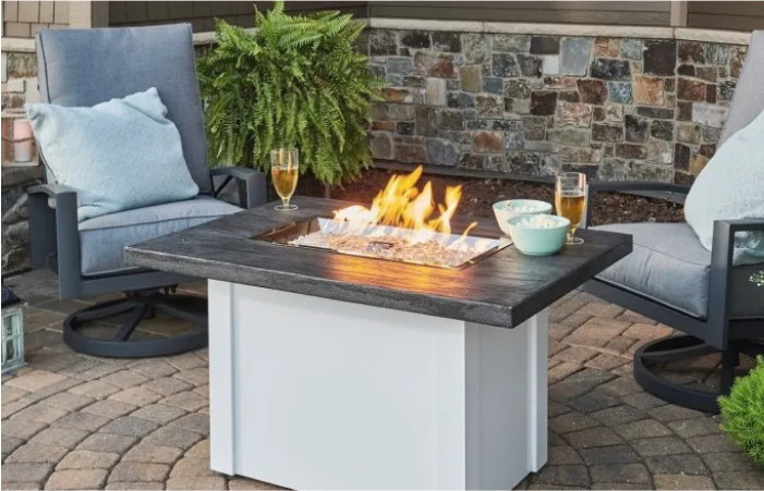 A fire pit is sitting on a patio next to two chairs.