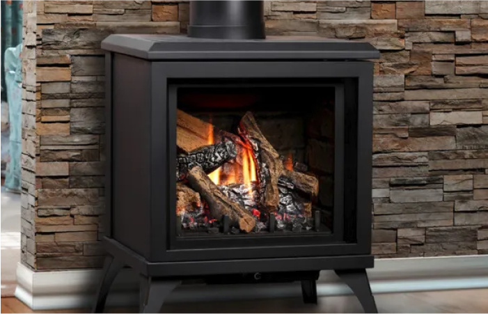 A gas fireplace is sitting in front of a stone wall.