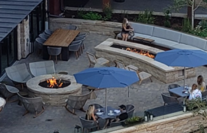 A group of people are sitting at tables in front of a fire pit.