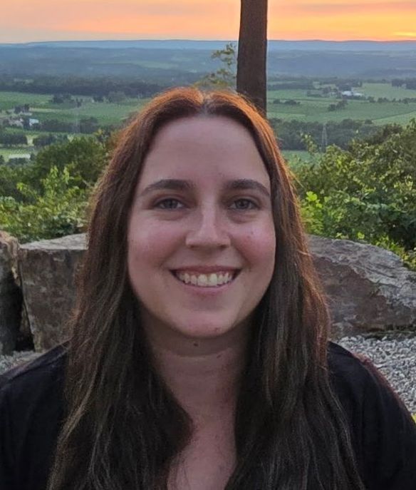 Woman smiling outdoors with a landscape backdrop at sunset.