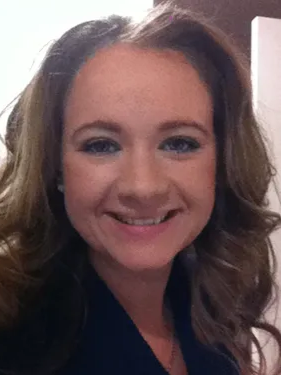 Woman with wavy brown hair smiles at the camera, wearing a dark blue top.