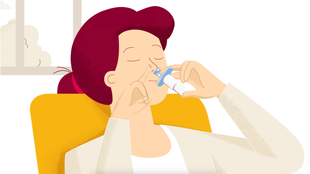 Woman using a nasal spray, sitting in a chair, eyes closed.