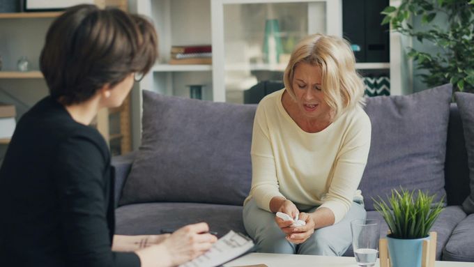 Woman in therapy, holding tissues, talking to therapist on sofa.