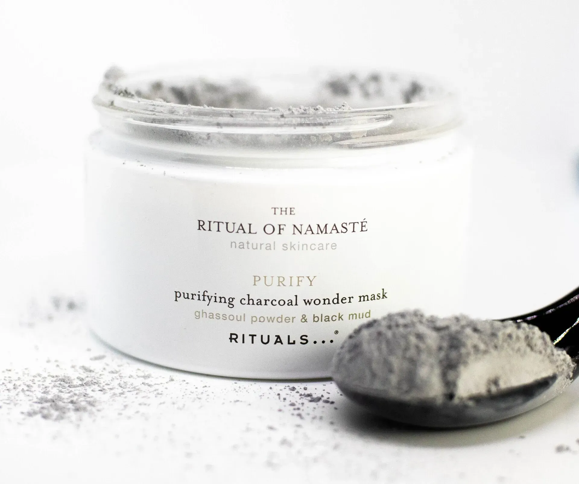 Jar of face mask powder with a spoonful of the product, gray and white.
