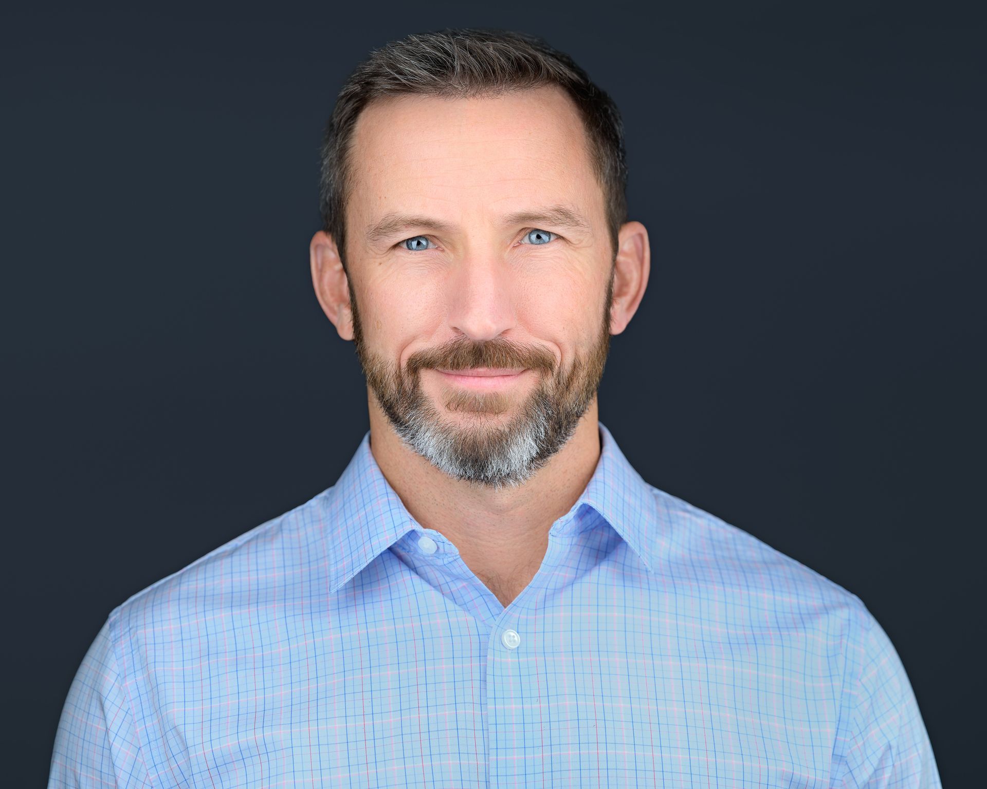 A man with a beard is wearing a blue shirt and smiling for the camera.