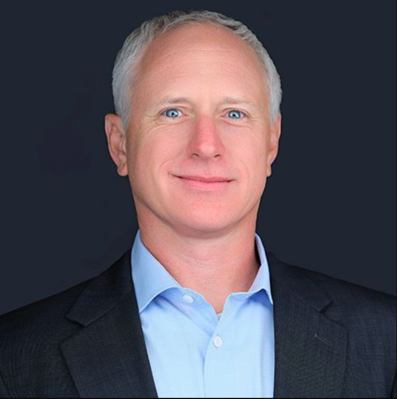 A man in a suit and blue shirt is smiling for the camera.