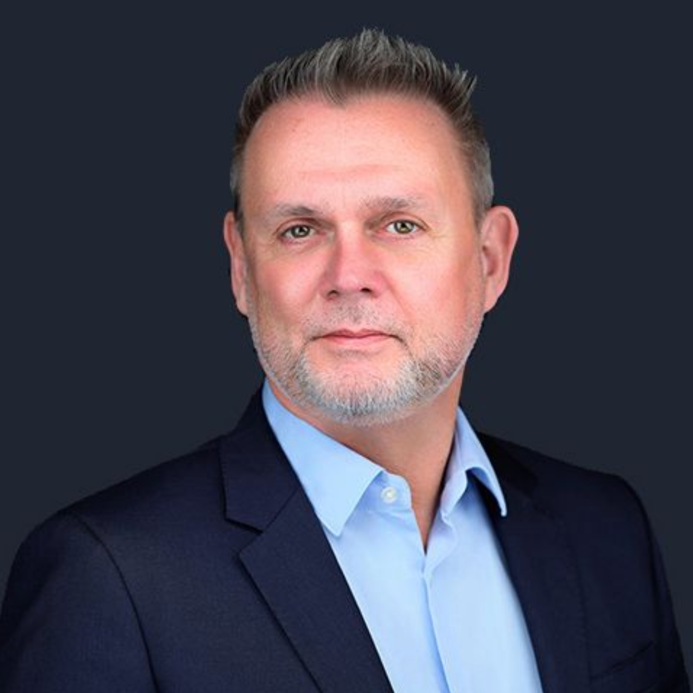 A man with a beard is wearing a suit and a blue shirt.