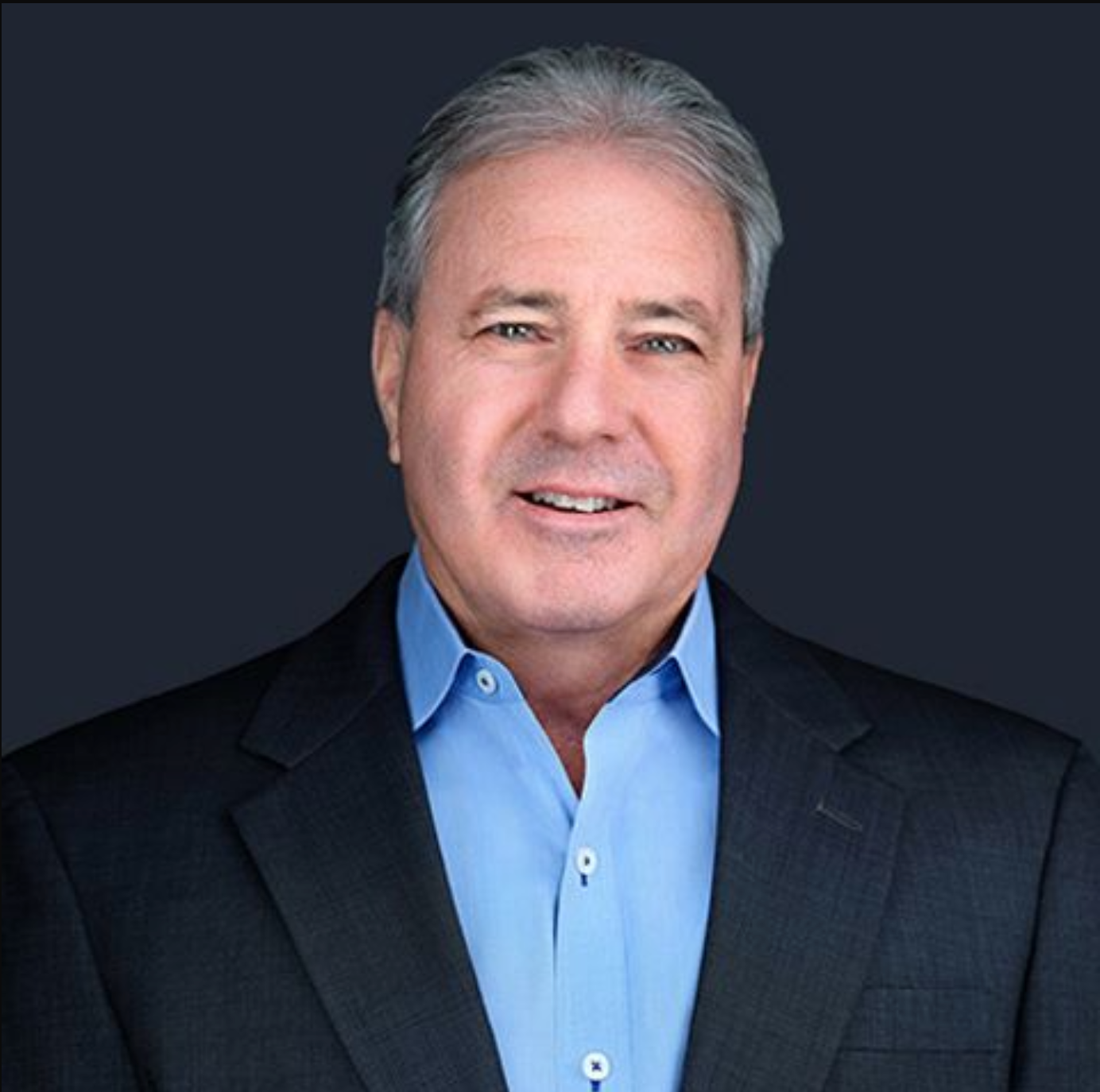 A man in a suit and blue shirt is smiling for the camera.