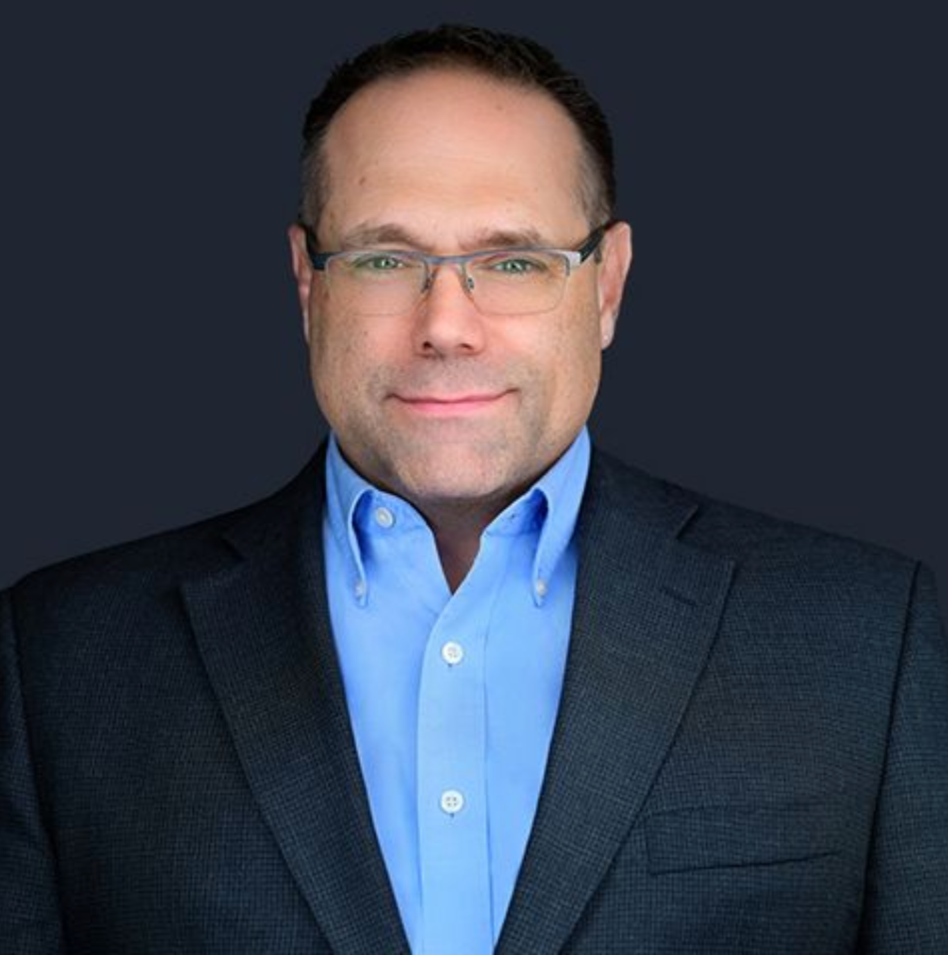 A man wearing glasses and a suit is smiling for the camera.