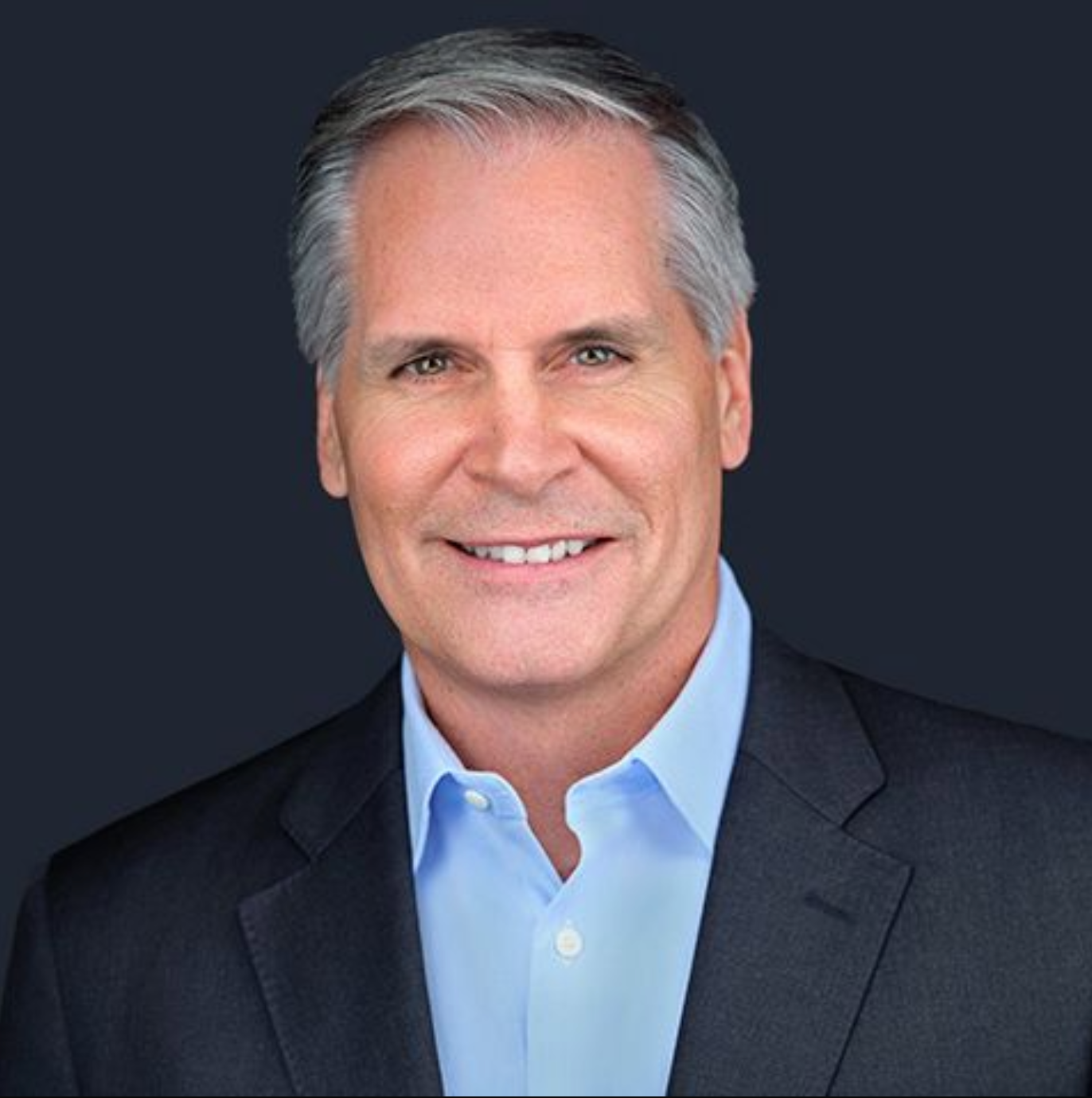 A man in a suit and blue shirt is smiling for the camera.