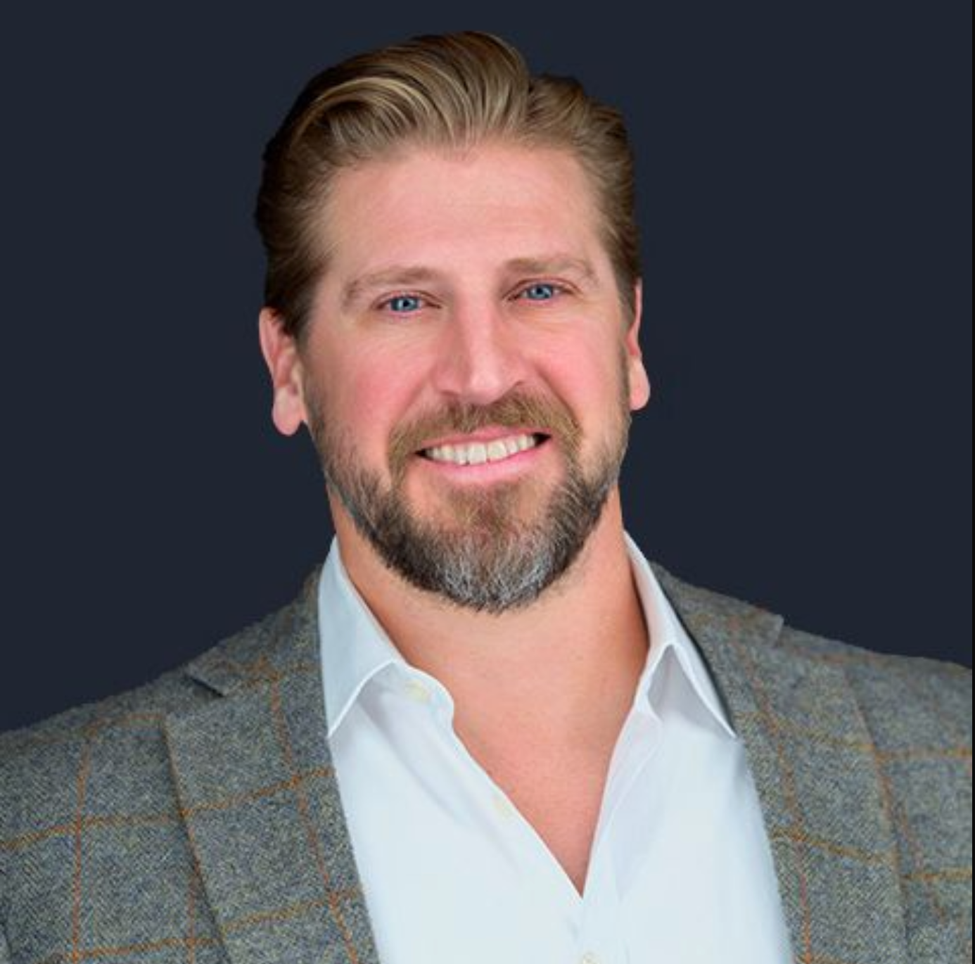 A man with a beard is wearing a suit and smiling.