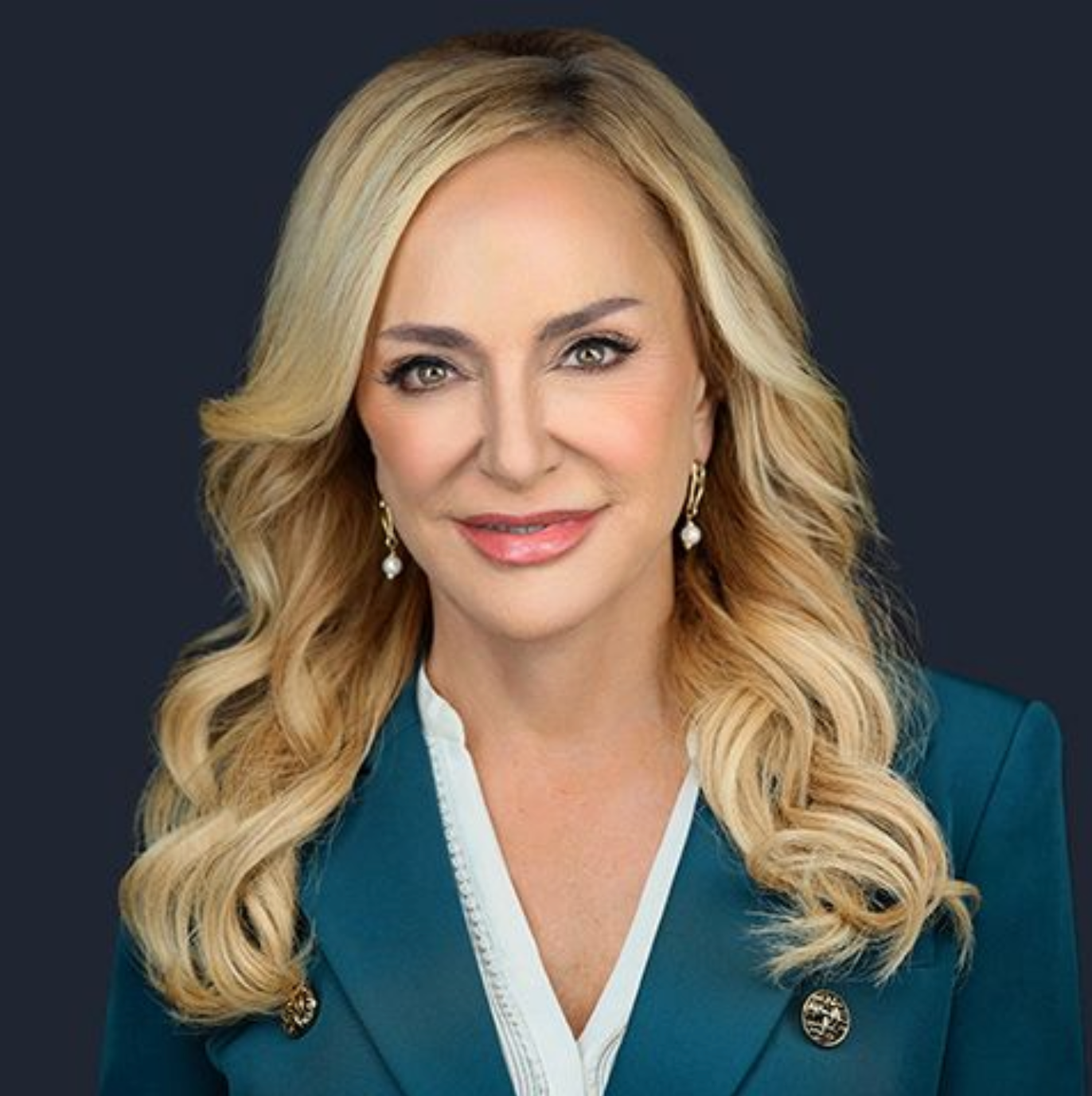 A woman with blonde hair is wearing a blue jacket and earrings.