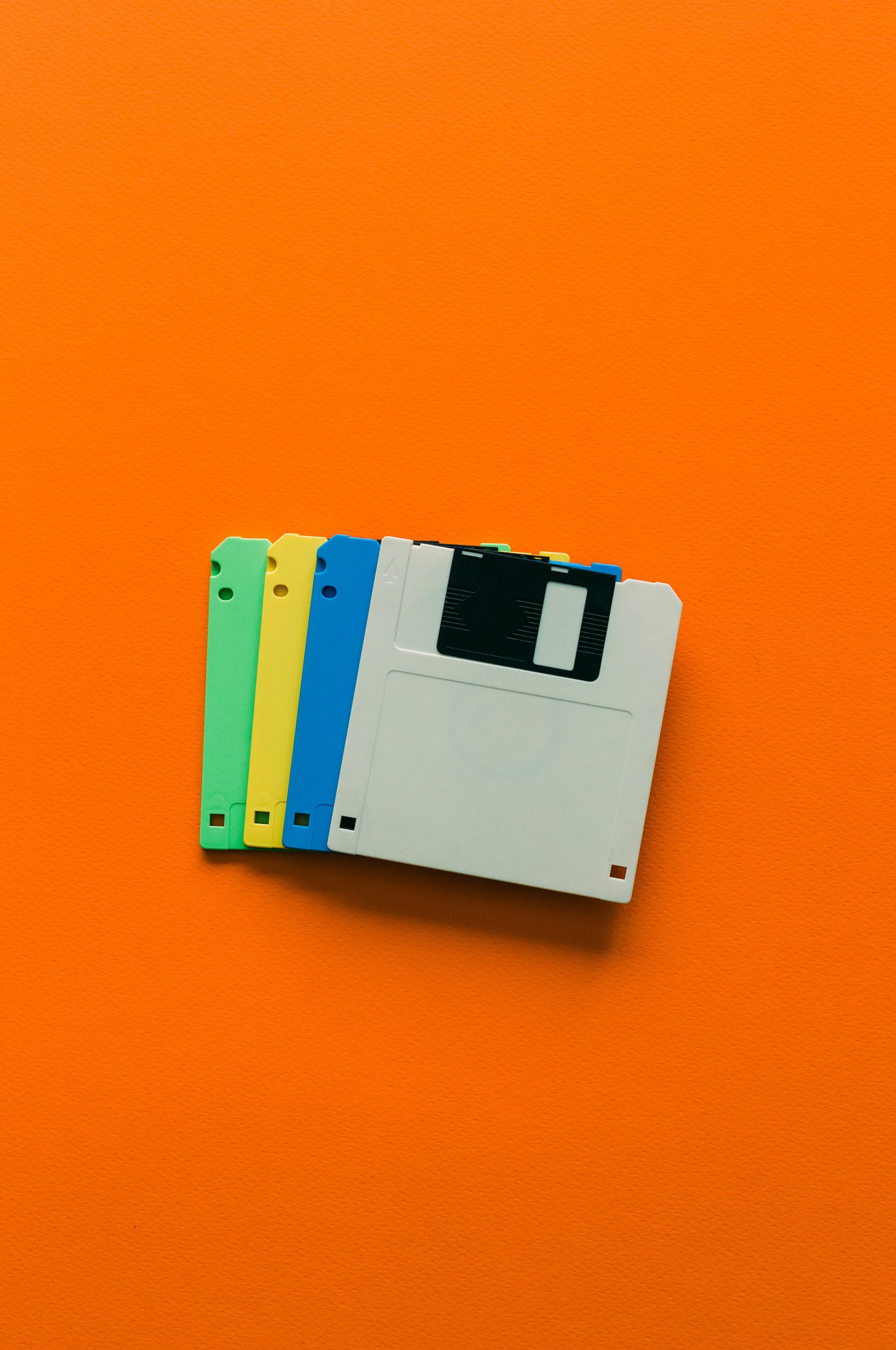 Four floppy discs of different colors are stacked on top of each other on an orange background.