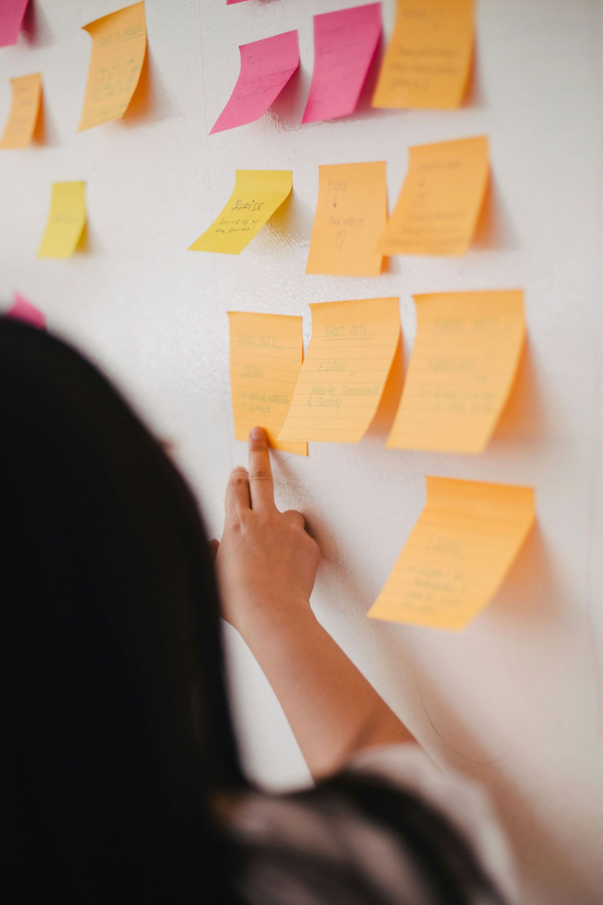 A woman is pointing at sticky notes on a whiteboard.