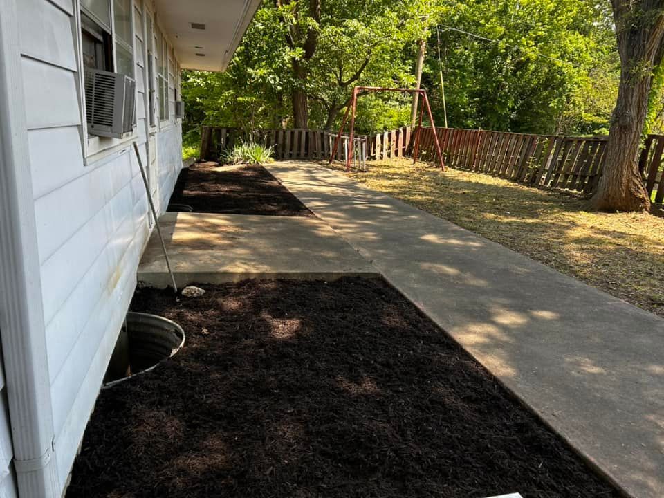 Side of a white house with fresh mulch beds along a concrete walkway, a swing set, and a fence.