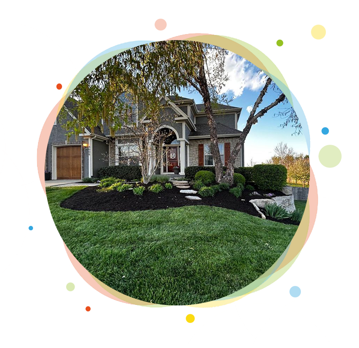 House with landscaped yard; green grass, black mulch beds, stone path, trees, and blue sky.