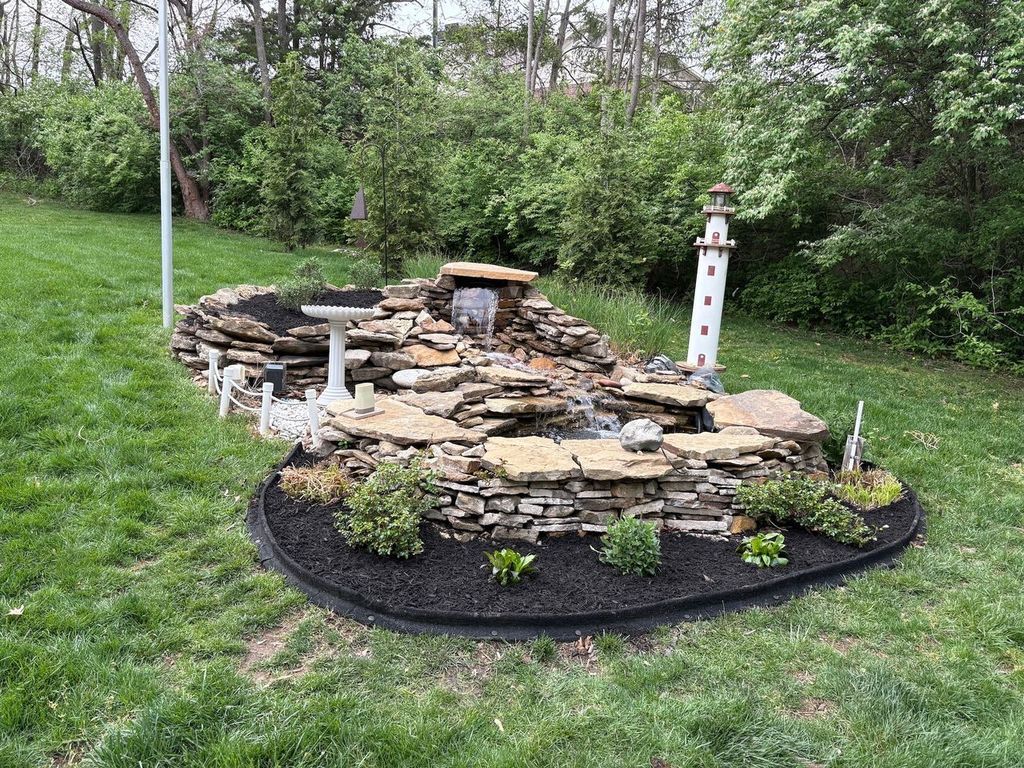 Stone waterfall feature with lighthouse and bird bath in a grassy yard.
