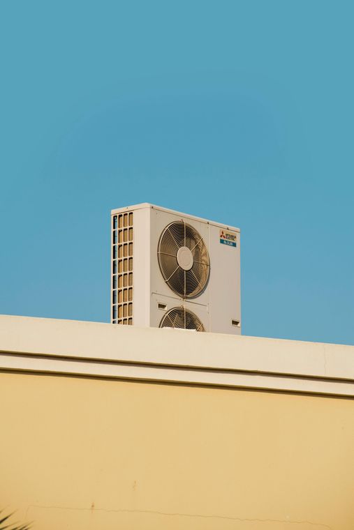 Air conditioning unit on a building's beige roof against a clear blue sky.
