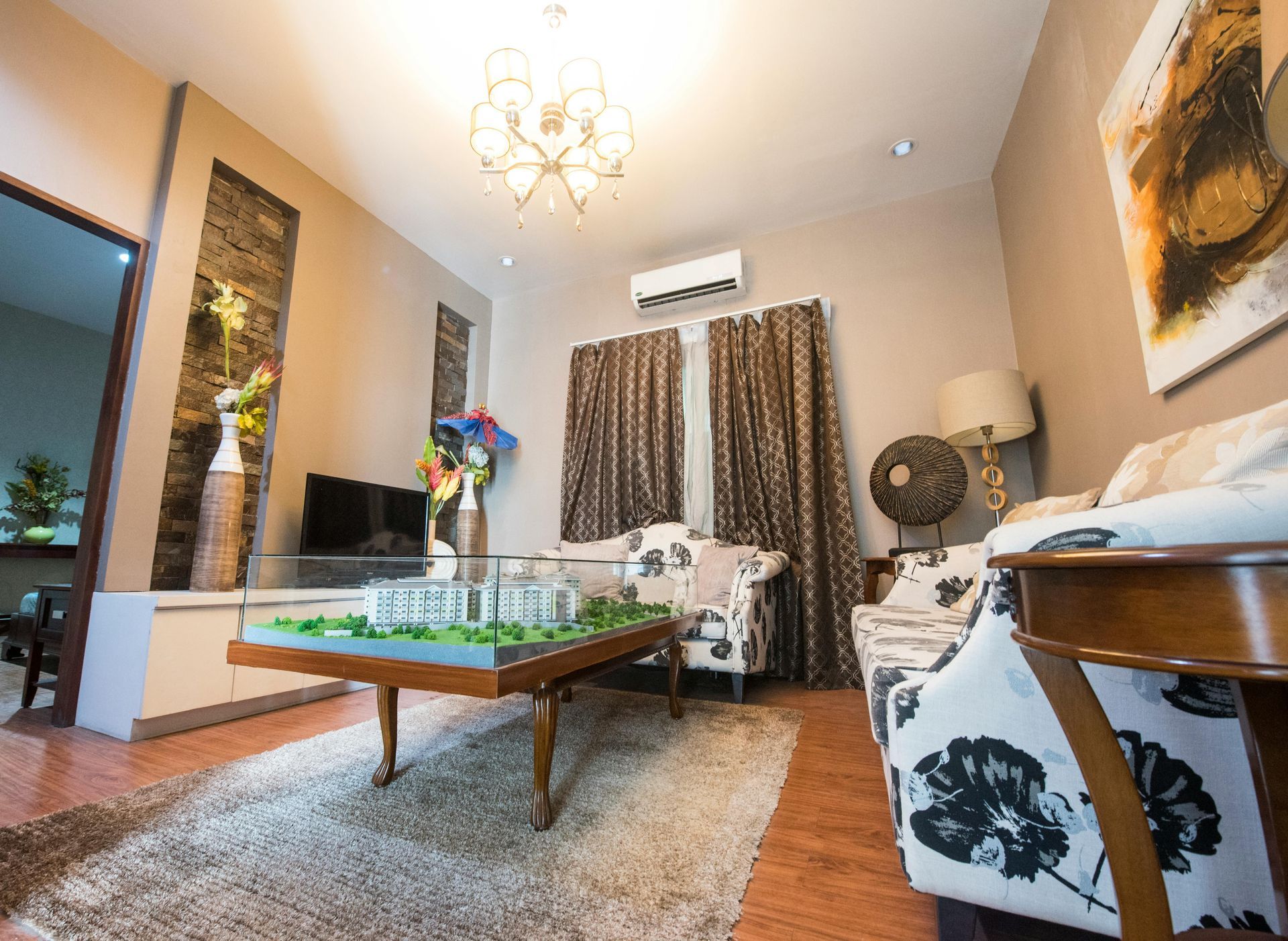 Living room with floral sofas, brown curtains, model on coffee table, and abstract art.