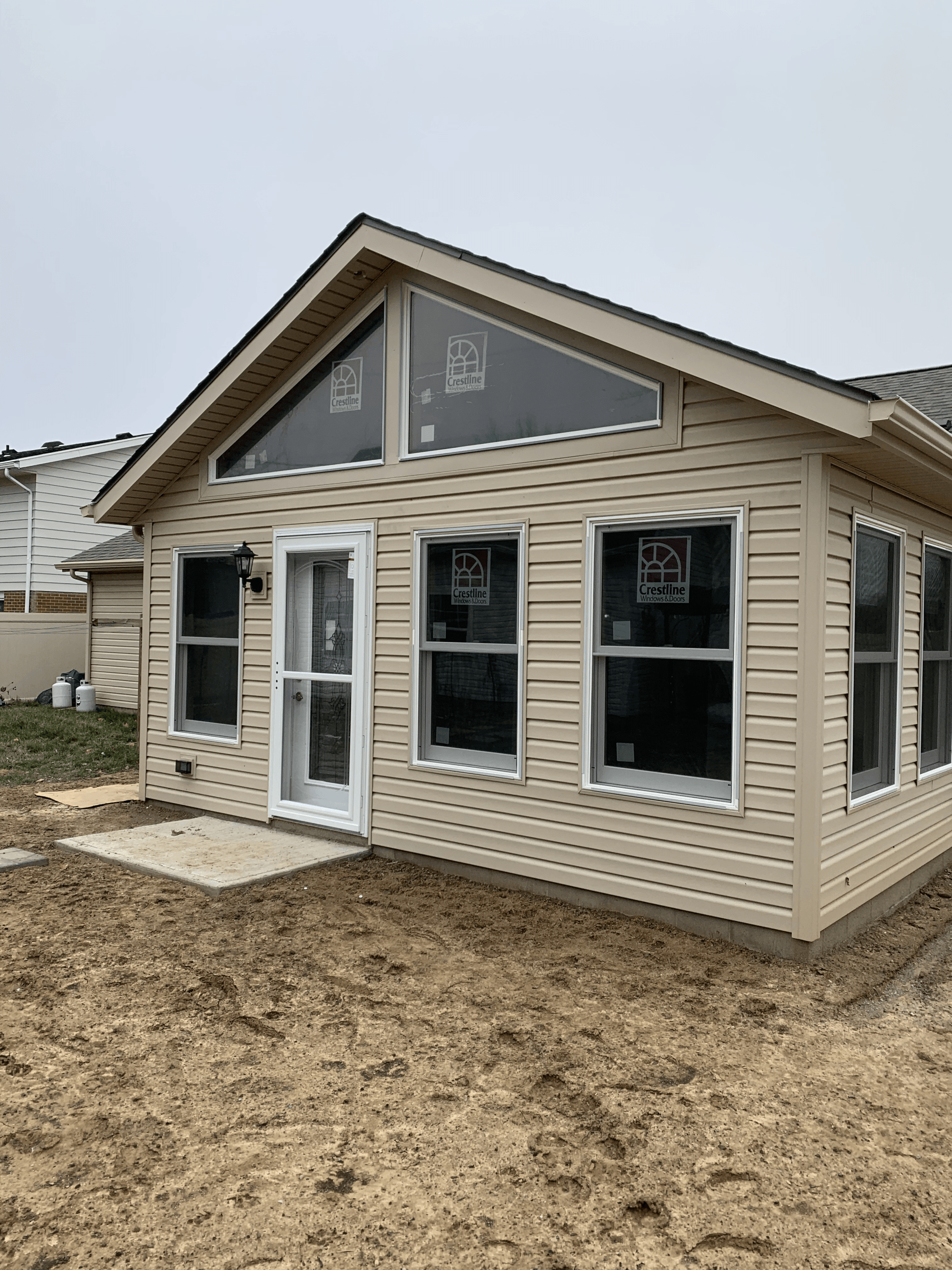 A small house with a lot of windows is sitting on top of a dirt field.