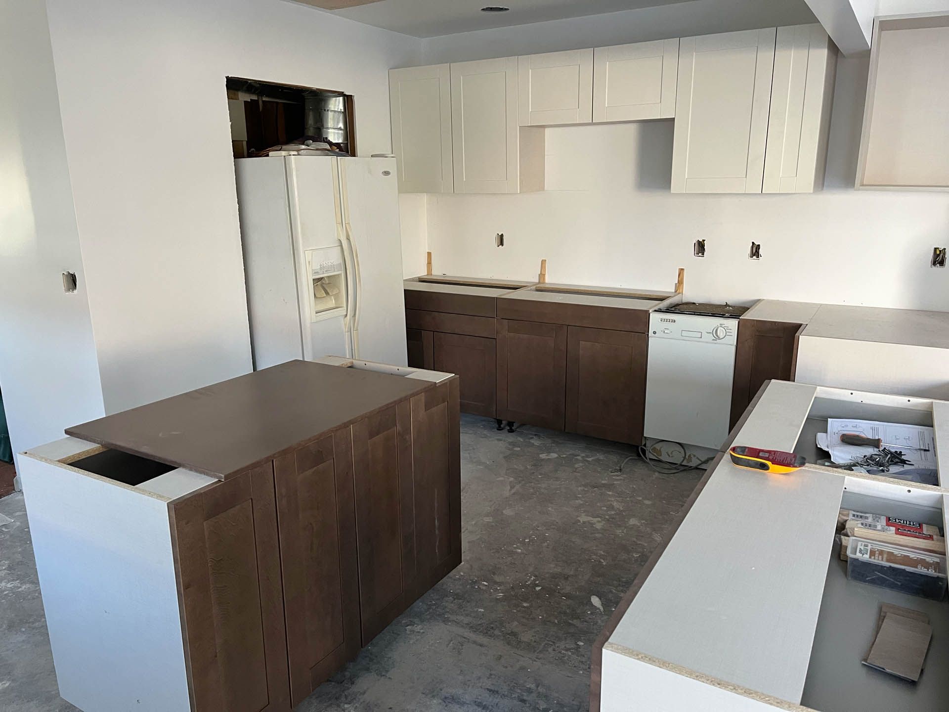 A kitchen under construction with white cabinets and a refrigerator