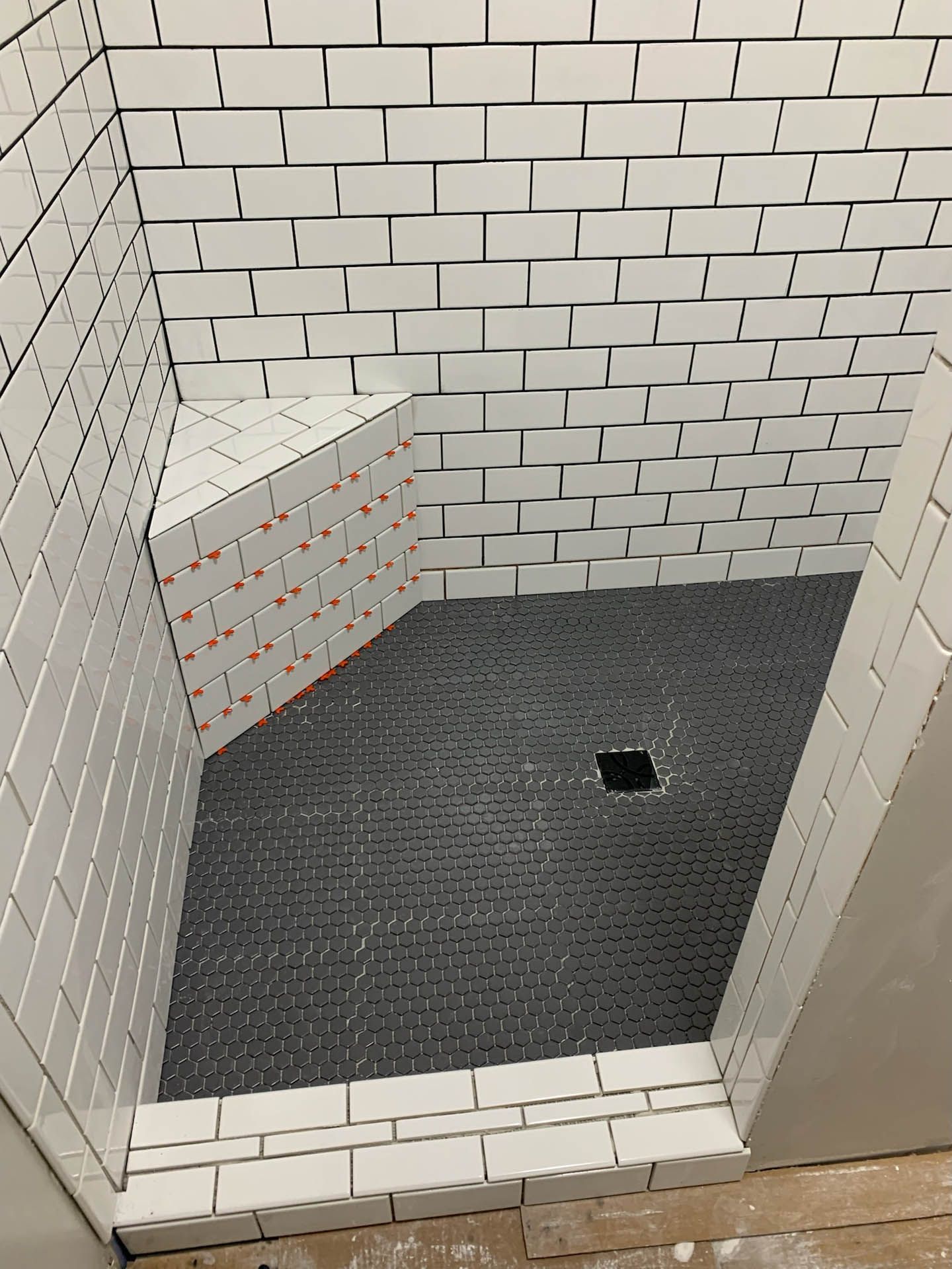 A shower stall with white tiles and a black tile floor.