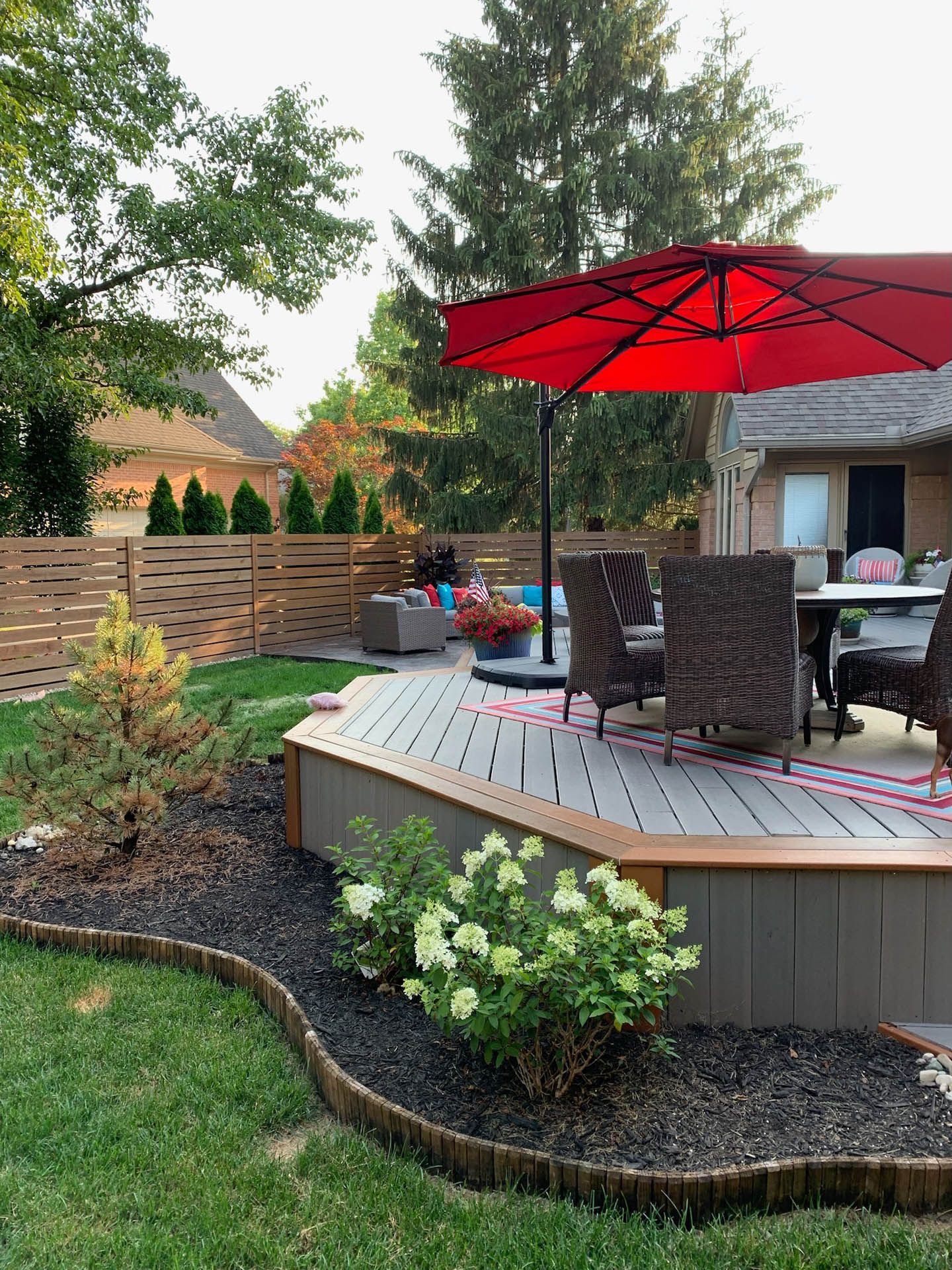 There is a red umbrella on the deck in the backyard.