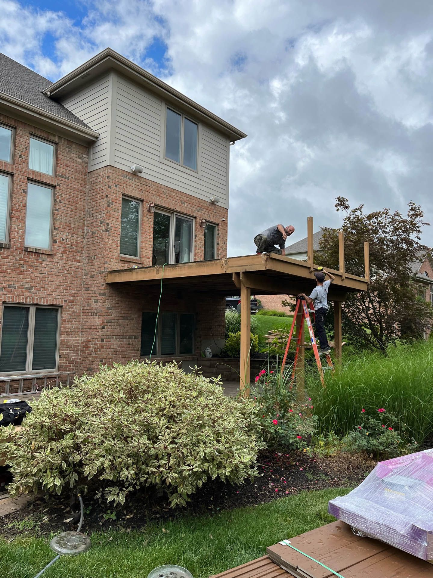 A man is standing on a wooden deck in front of a brick house.
