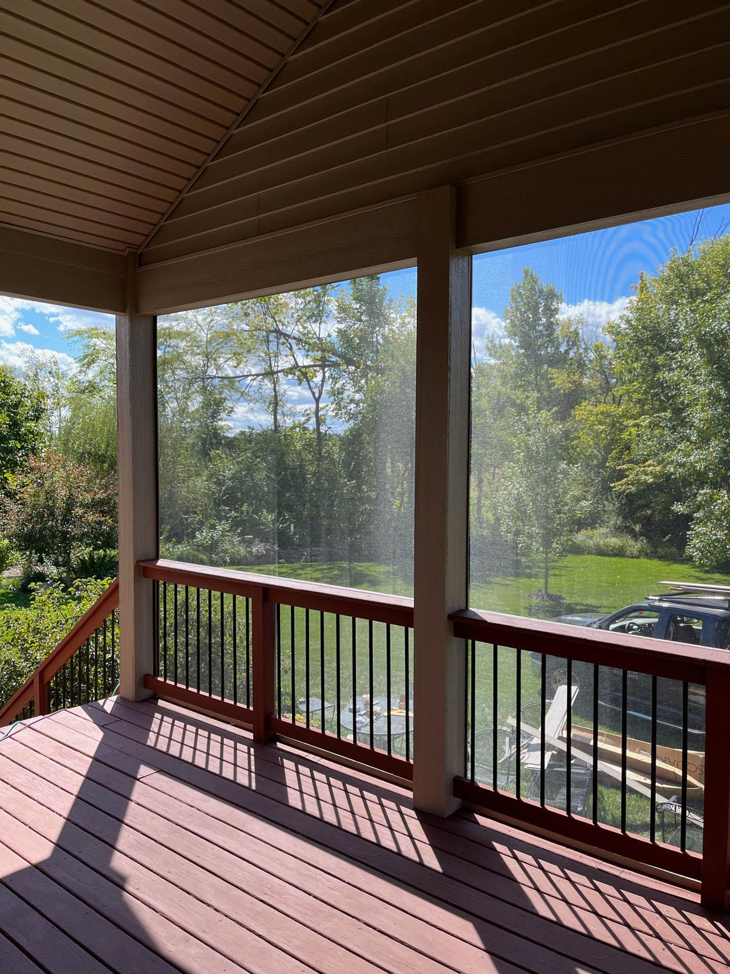 A screened in porch with a view of a lush green field and trees.