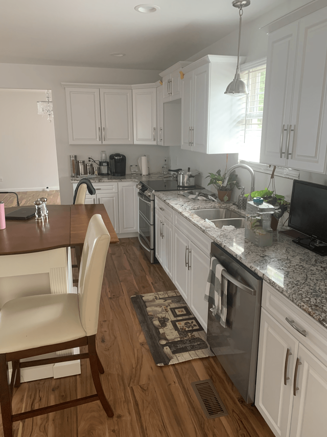 A kitchen with white cabinets , granite counter tops , stainless steel appliances , a table and chairs.