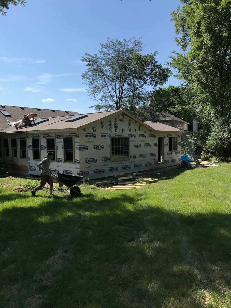 A man is pushing a wheelbarrow in front of a house under construction.
