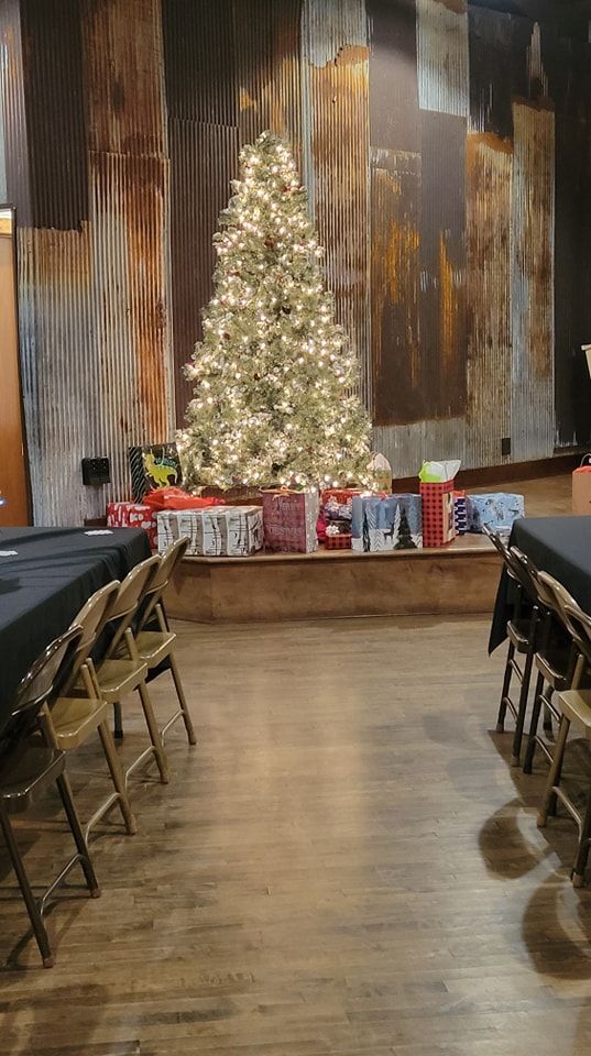 There is a christmas tree in the middle of a room with tables and chairs.