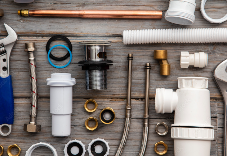 Plumbing tools and parts arranged on a weathered wooden surface, including wrenches, pipes, and fittings.