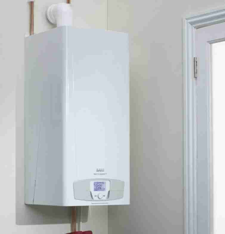 White wall-mounted gas boiler with digital display and copper pipes, near a white door frame.