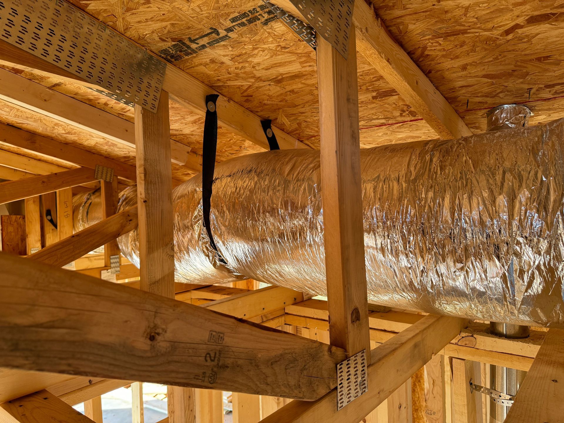 A large duct is hanging from the ceiling of a house under construction.