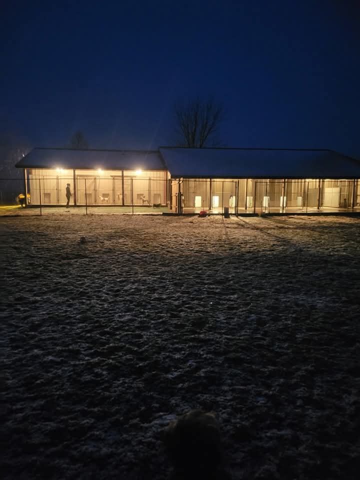 Long, modern building lit up at night, set on frosty grass field.
