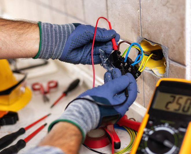 An electrician is working on an electrical outlet with a multimeter