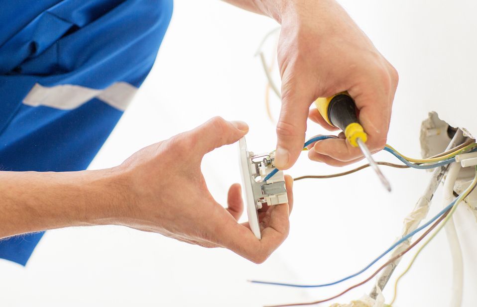 A man is fixing an electrical outlet with a screwdriver