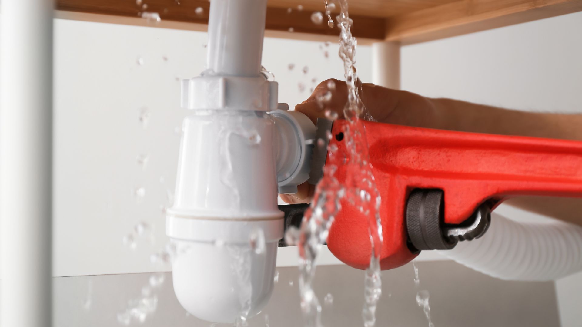 A person is fixing a leaking sink pipe with a wrench.