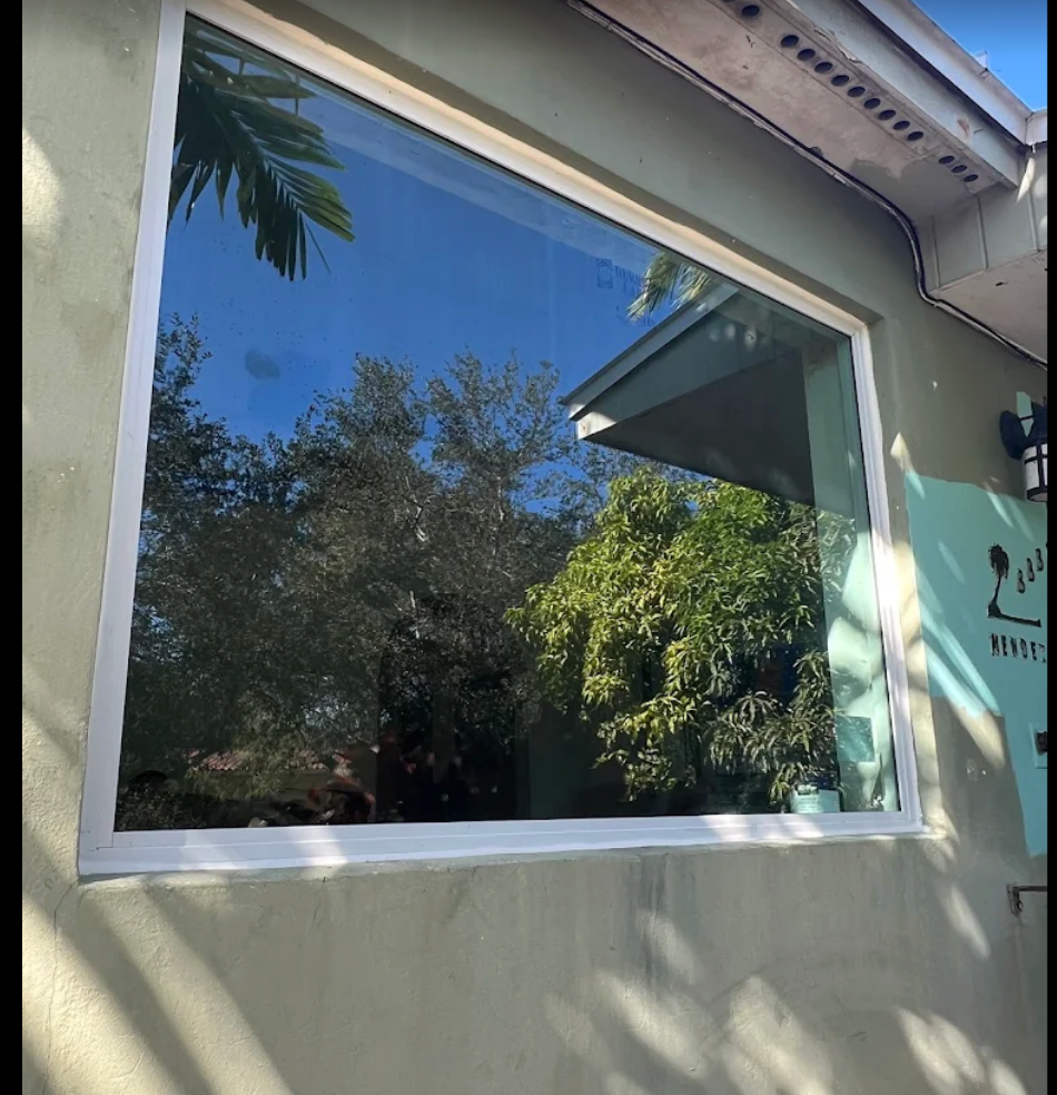 Large rectangular window reflecting trees and a blue sky in a light green building.