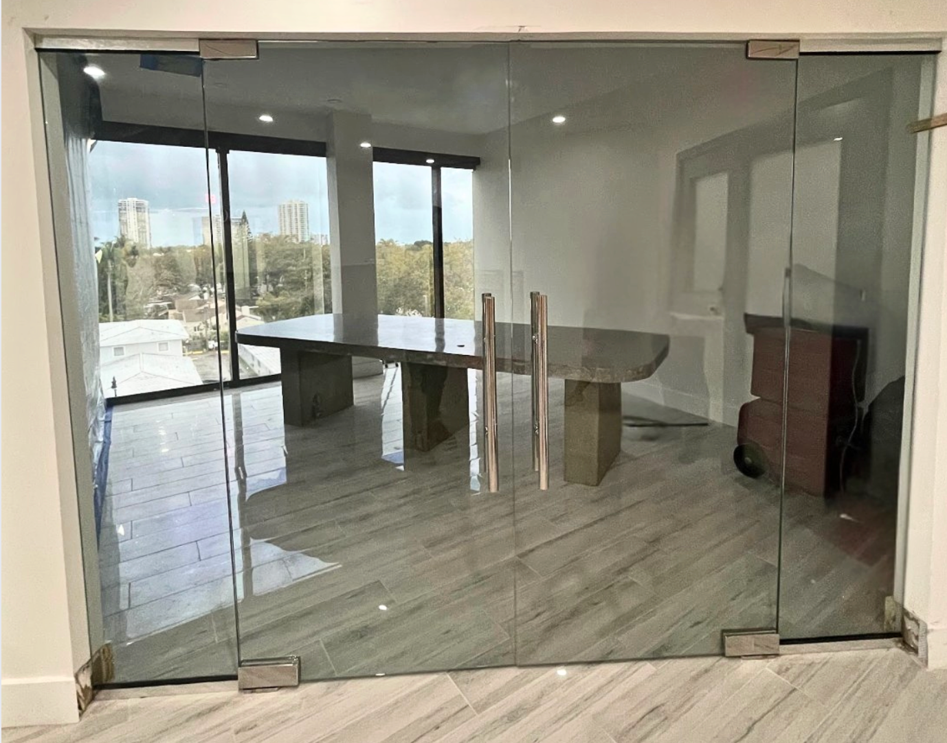 Glass-walled office with a large table, modern decor, and cityscape views visible through windows.