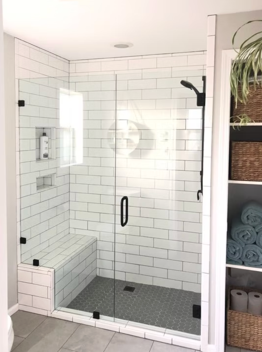 Modern bathroom with glass shower, subway tile walls, built-in bench, and black fixtures.