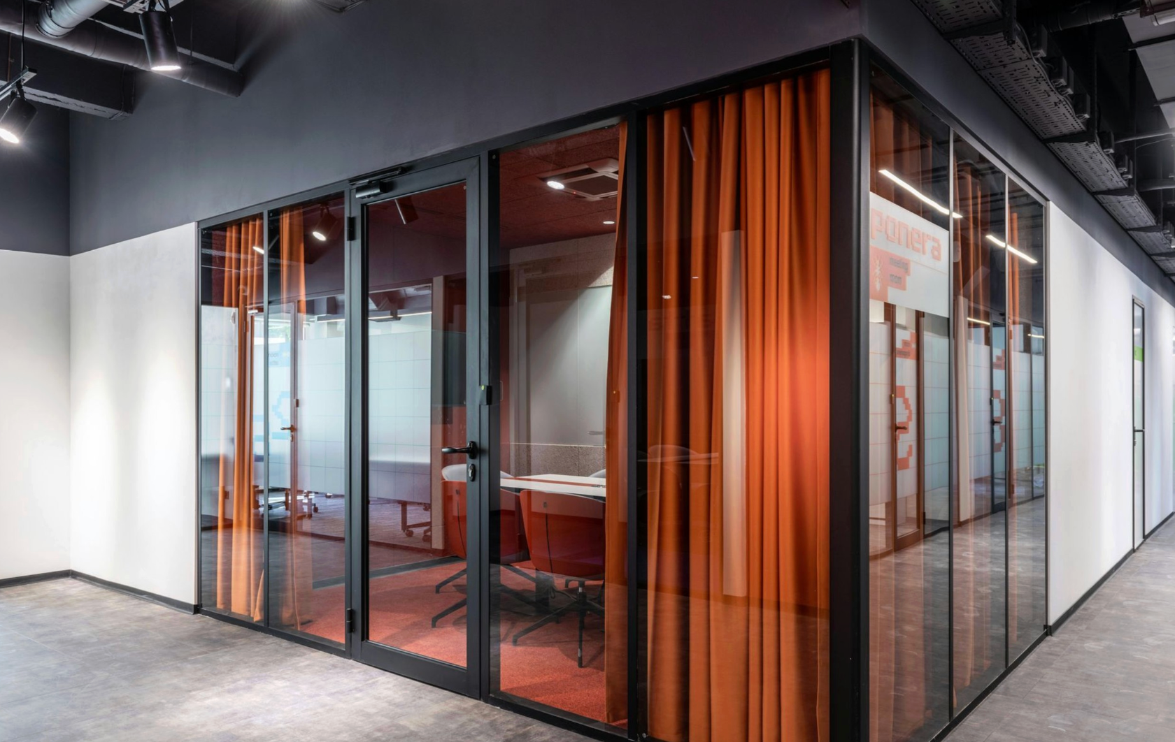 Glass-walled office space with orange curtains. Dark frames and ceiling, white walls, and a corridor.