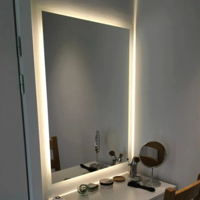 Lit rectangular vanity mirror with a white frame above a white table with makeup items.