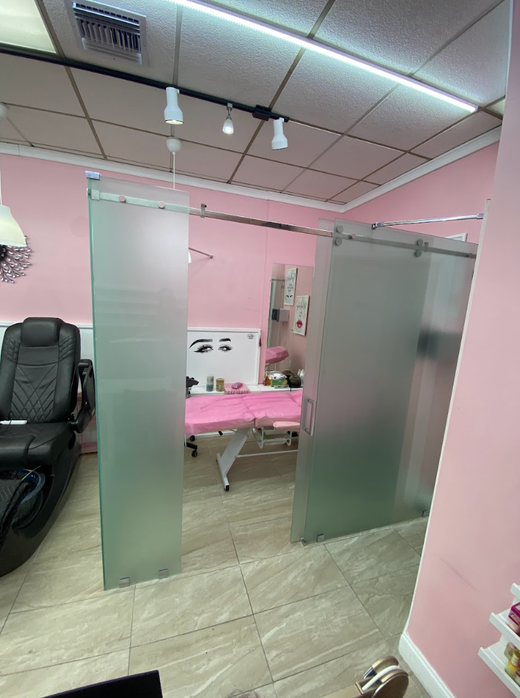 Interior of a beauty salon with pink walls and frosted glass sliding doors. A black chair and a treatment table are visible.