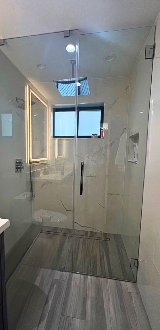 Modern bathroom with glass shower enclosure, marble walls, and wood-look tile flooring.