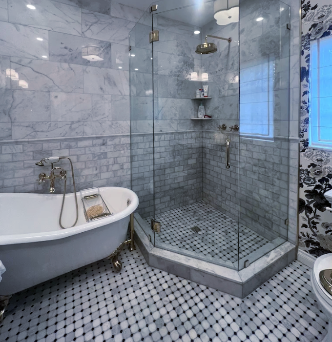 Bathroom with a claw-foot tub and glass shower; gray marble walls and penny tile floor.